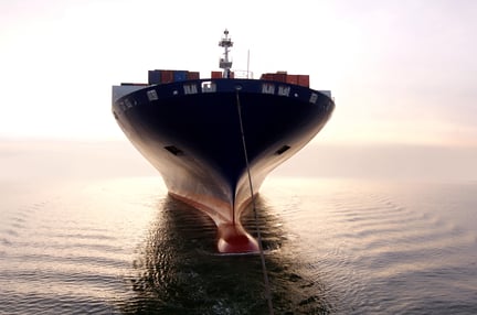 A cargo ship loaded with containers sits calmly on the water at sunrise, representing global maritime logistics.